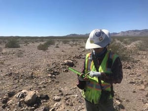 Biologist in hat and safety vest collecting field data on mobile device in the desert.